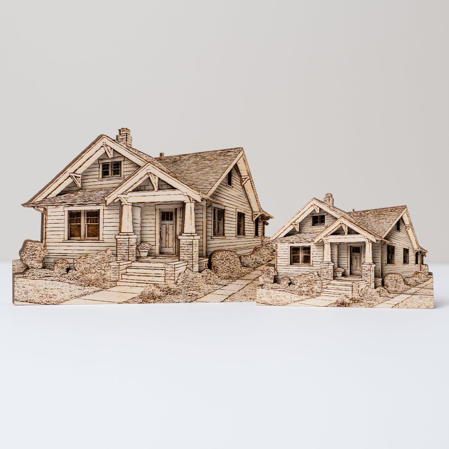 Wooden model of a two-story house with a smaller one of the same design for size comparison on a white background