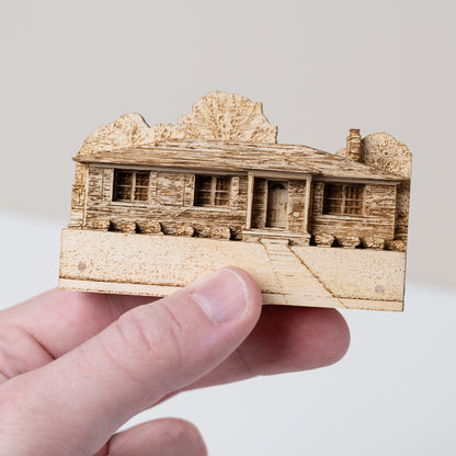 Hand holding a small sized wooden model of a house against a plain background
